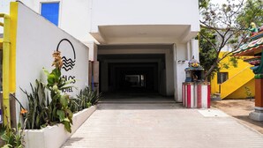 Entrada de hotel con un letrero, un camino de hormigón y un edificio colorido al fondo.