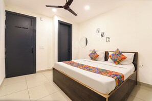 A bedroom with a bed, two doors, a ceiling fan, a mirror, and a wall with framed pictures.