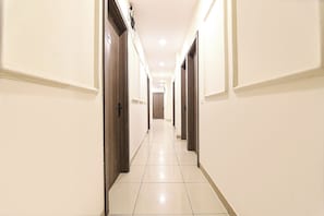 A hotel hallway with doors on both sides, a tiled floor, and a light fixture on the ceiling. - Via Ak Residency (New Delhi)