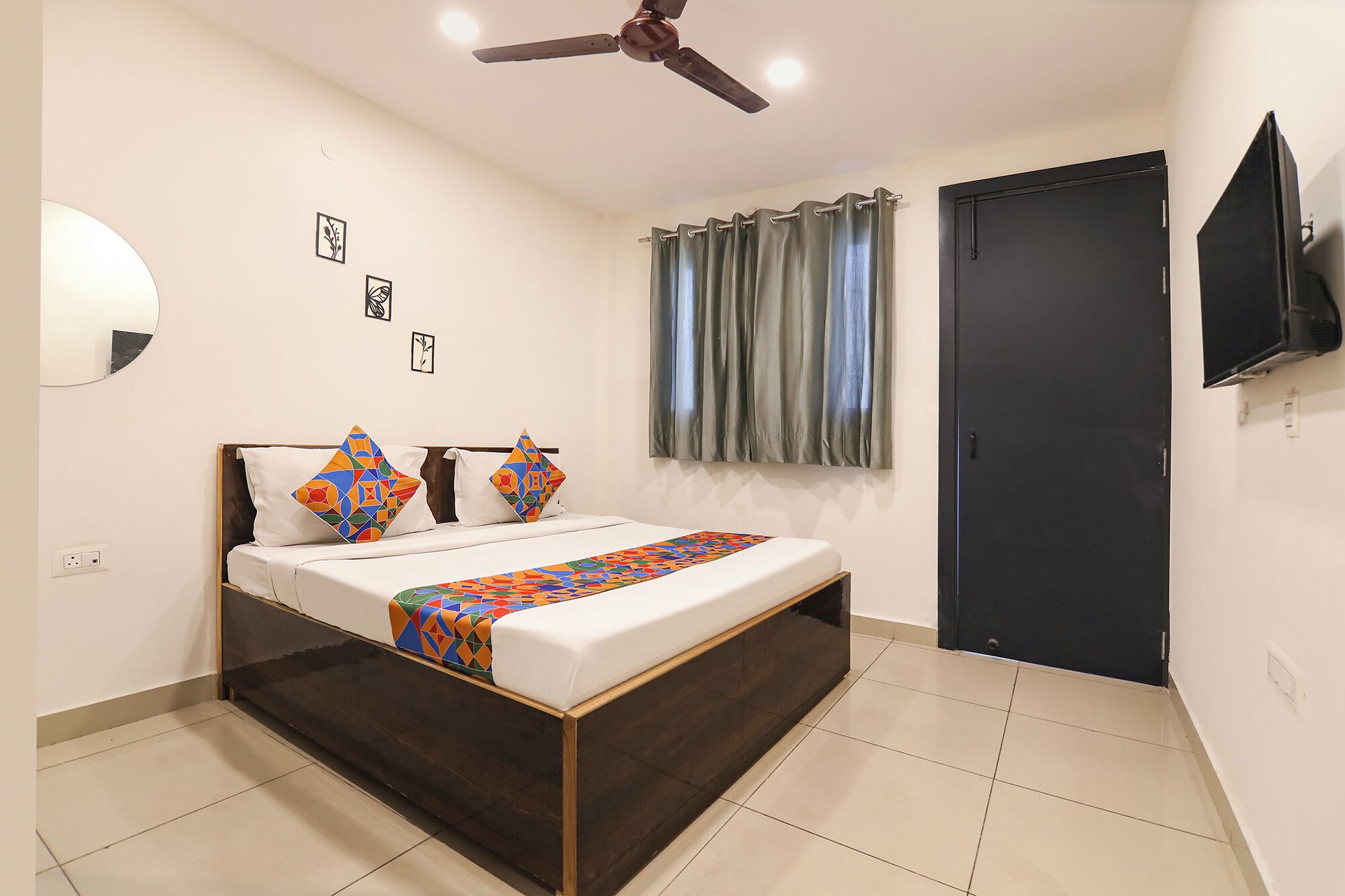 A bedroom with a bed, a ceiling fan, a TV, and a door.