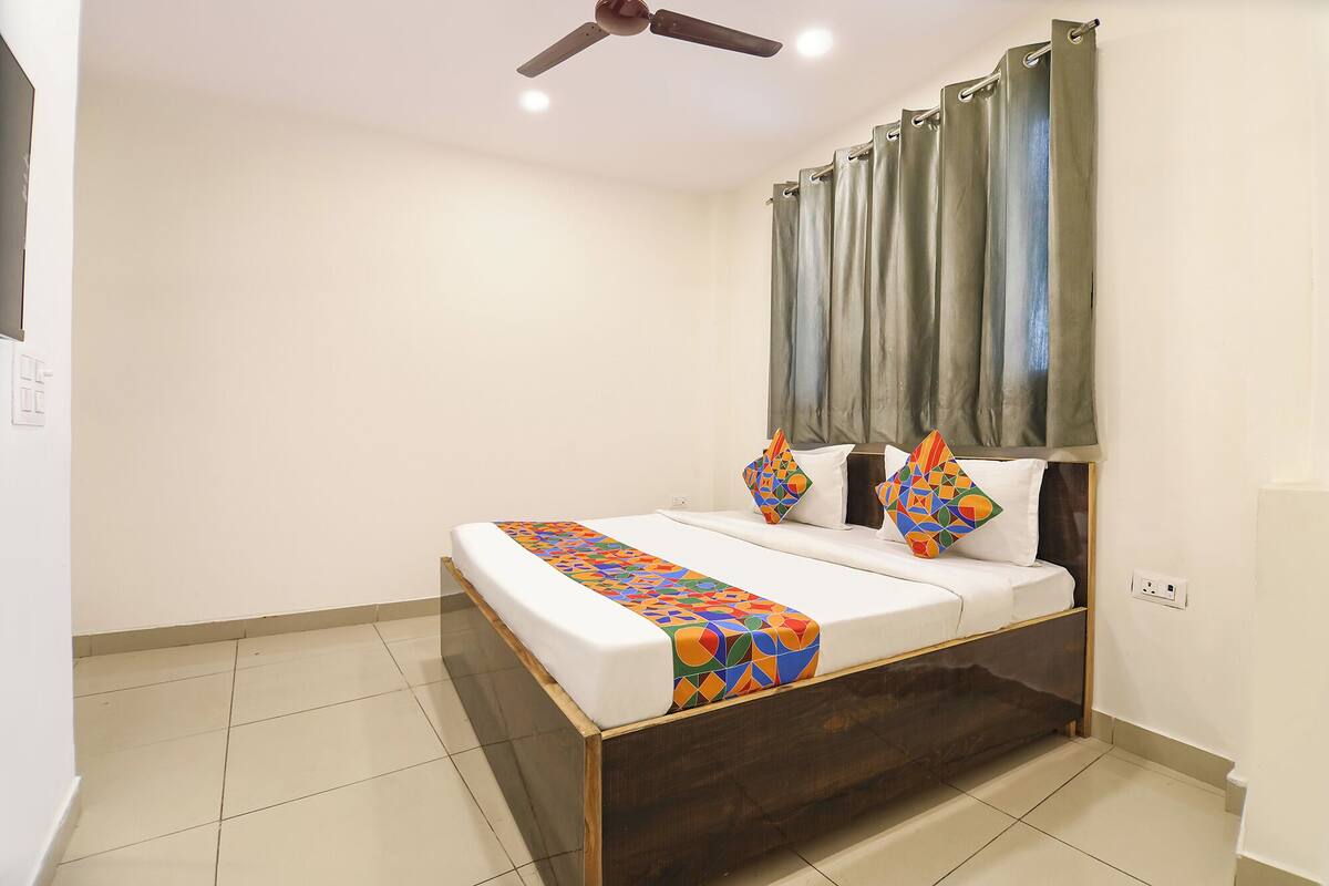Quarto de hotel com cama, ventoinha no teto, janela com cortinas e chão de azulejos.