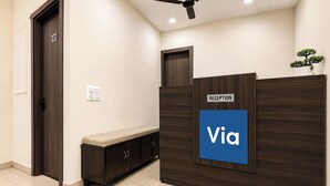 A reception desk with a 'Via' sign, a dark wooden bench, a door labeled '101', and a small plant on top. - Via Ak Residency (New Delhi)