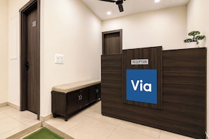 A reception desk with a 'Via' sign, a dark wooden bench, a door labeled '101', and a small plant on top. - Via Ak Residency (New Delhi)