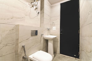 A bathroom with a white toilet, a sink, and a shower. - Via Ak Residency (New Delhi)