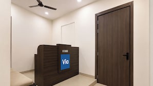 A reception desk with a sign, a closed door, and a ceiling fan. - Via Ak Residency (New Delhi)