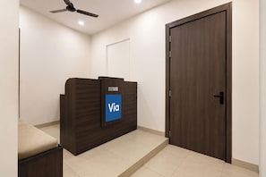 A reception desk with a sign, a closed door, and a ceiling fan. - Via Ak Residency (New Delhi)