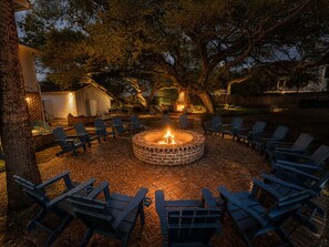 A circular fire pit surrounded by chairs, with trees and a building in the background. - Private Luxury Estate Steps to the Beach | Heated Pool Access (Tybee Island)