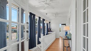 Eine überdachte Veranda mit weißen Geländern, einem Deckenventilator und einem Tisch mit Lampe.