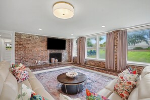 A living room with a brick wall, a fireplace, a large window, and a round coffee table.