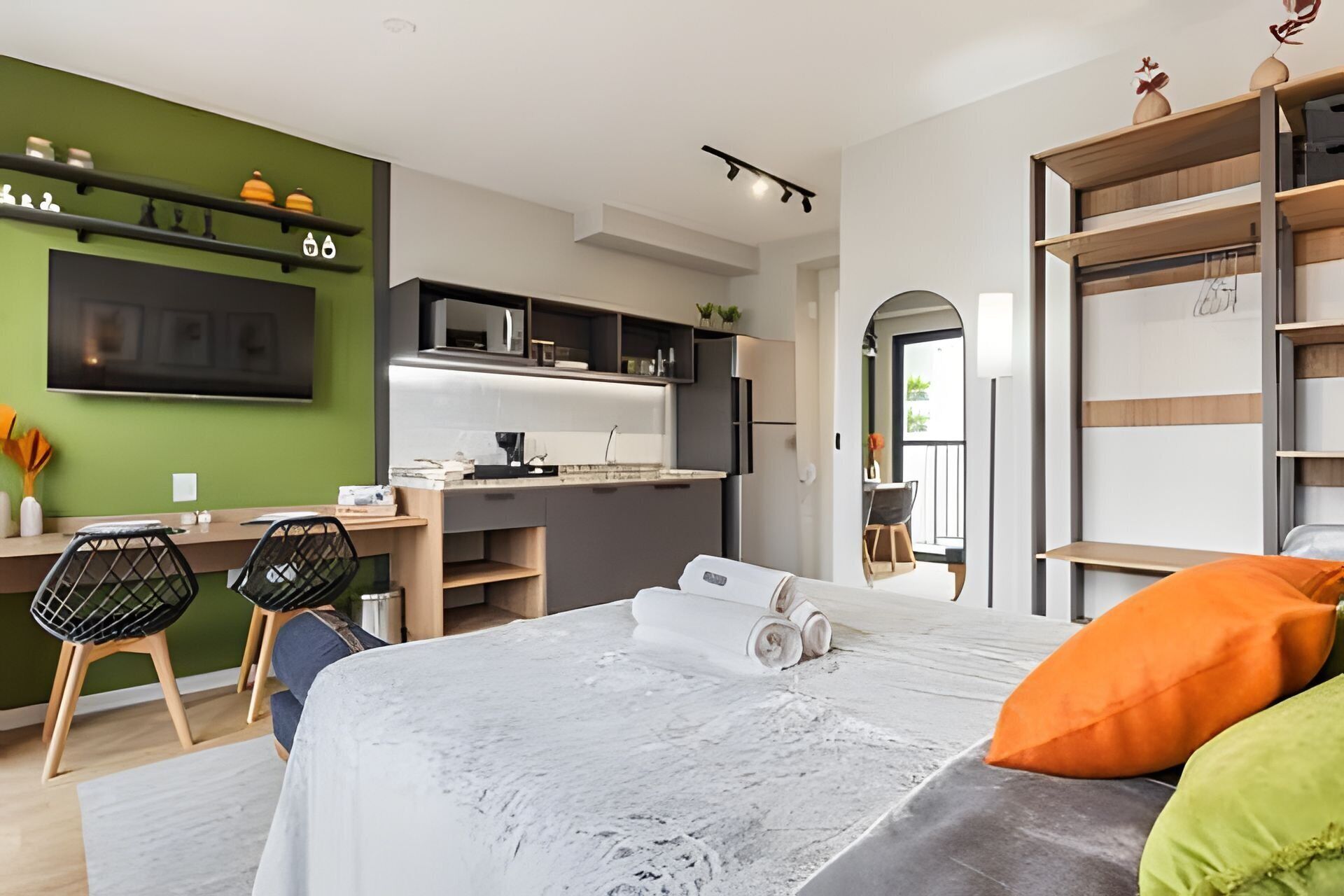 Una habitación de hotel moderna con kitchenette, una cama con almohadas y un escritorio con sillas.