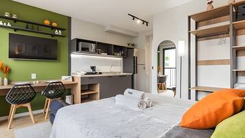Una habitación de hotel moderna con kitchenette, una cama con almohadas y un escritorio con sillas.