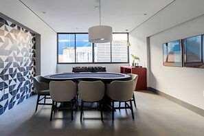 Ein moderner Besprechungsraum mit rundem Tisch, sechs Stühlen, einem roten Akzent und einem großen Fenster mit Blick auf die Stadt.