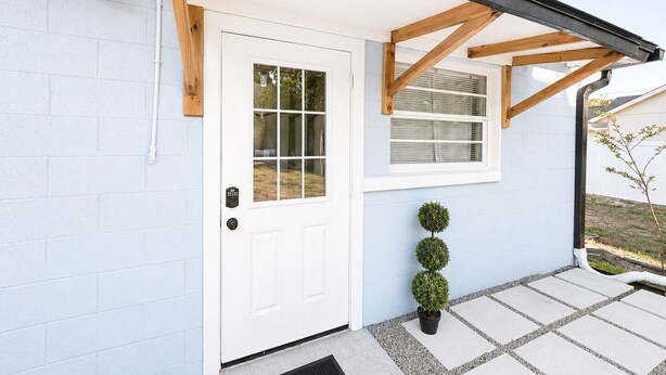 Une maison avec une porte blanche, une petite fenêtre et un pot de fleurs.