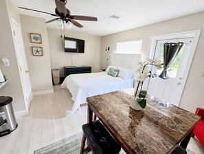 Un dormitorio con cama, escritorio, ventilador de techo, televisor y ventana con cortinas.