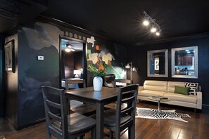 A modern living room with a dining area, featuring a sofa, a dining table with chairs, a zebra rug, and a large abstract painting on the wall. - Your TMC Flats! Sleeps 32, 16BR, 8BA, 8PA (Houston)