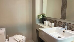 Ein Badezimmer mit Toilette, Waschbecken, Spiegel und einer Blumenvase.