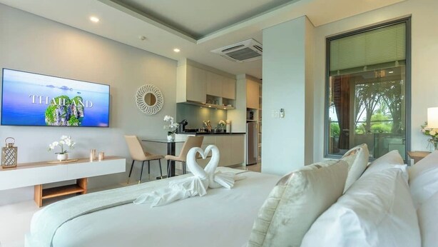 Ein modernes Hotelzimmer mit Bett, Fernseher, Schreibtisch und Blick auf die Küche.