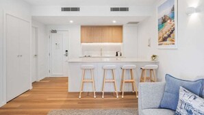 A modern kitchen with white cabinets, a central island with stools, and a dining area with a sofa and a painting.