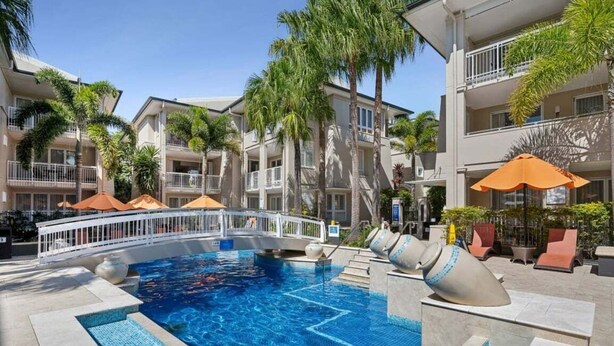 A swimming pool with a bridge, palm trees, and outdoor seating.