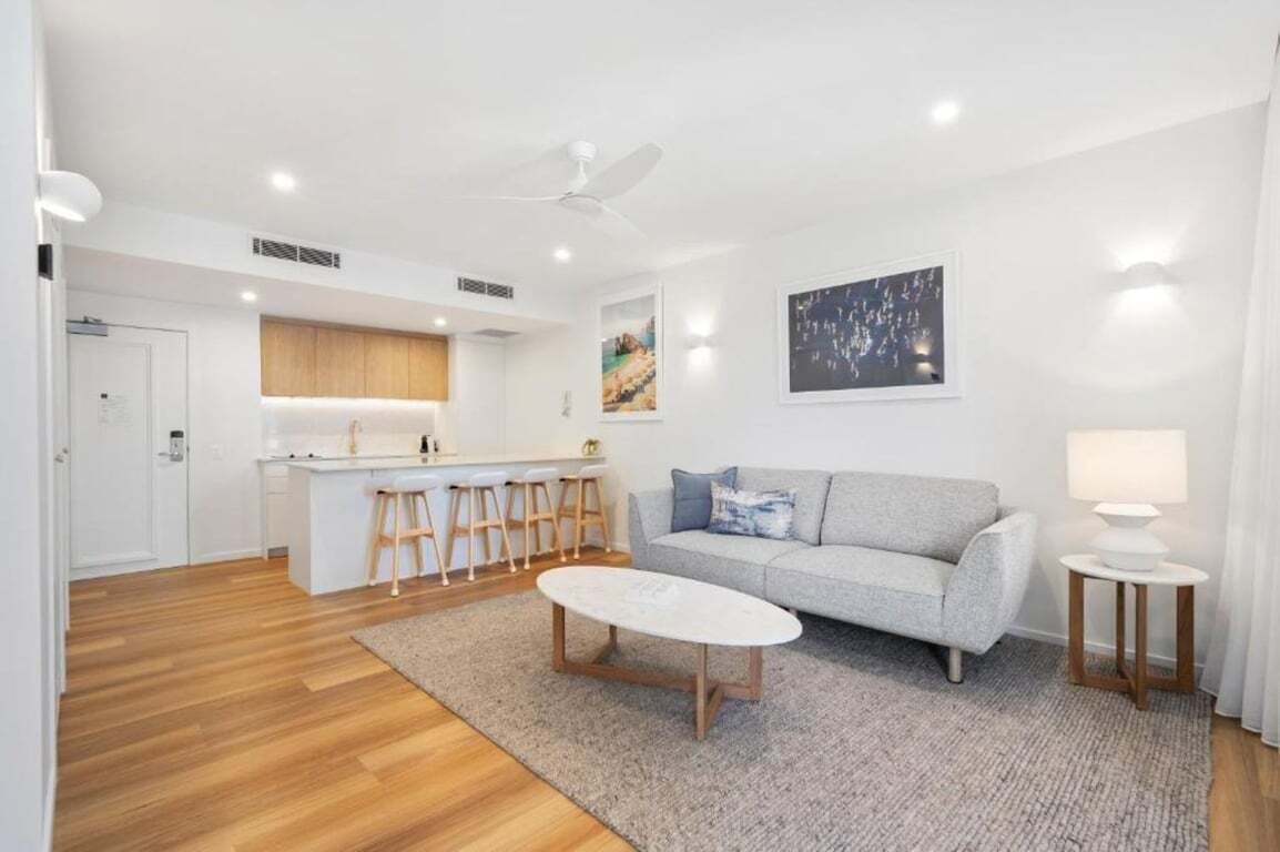 A modern living room with a sofa, coffee table, and a kitchen area with stools.