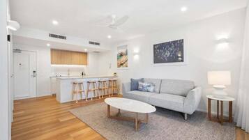 A modern living room with a sofa, coffee table, and a kitchen area with stools.