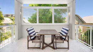 A balcony with a table and chairs, a view of greenery, and a white railing.