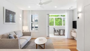 A modern living room with a sofa, a small round table, a ceiling fan, and a TV mounted on the wall.