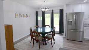 A dining area with a round table surrounded by chairs, a chandelier, and a refrigerator. - Creekside Corner (Bloomington)
