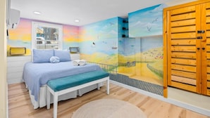 Un dormitorio con cama, banqueta y un mural de un paisaje con aves.
