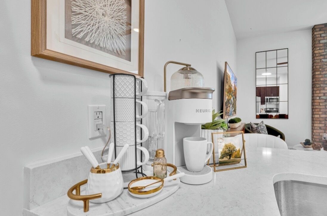 A modern kitchen with a coffee maker, white mugs, and a framed picture on the counter.