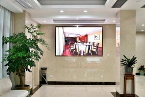 Un vestíbulo con una televisión de pantalla plana grande, una planta en maceta, un sofá y una mesita.