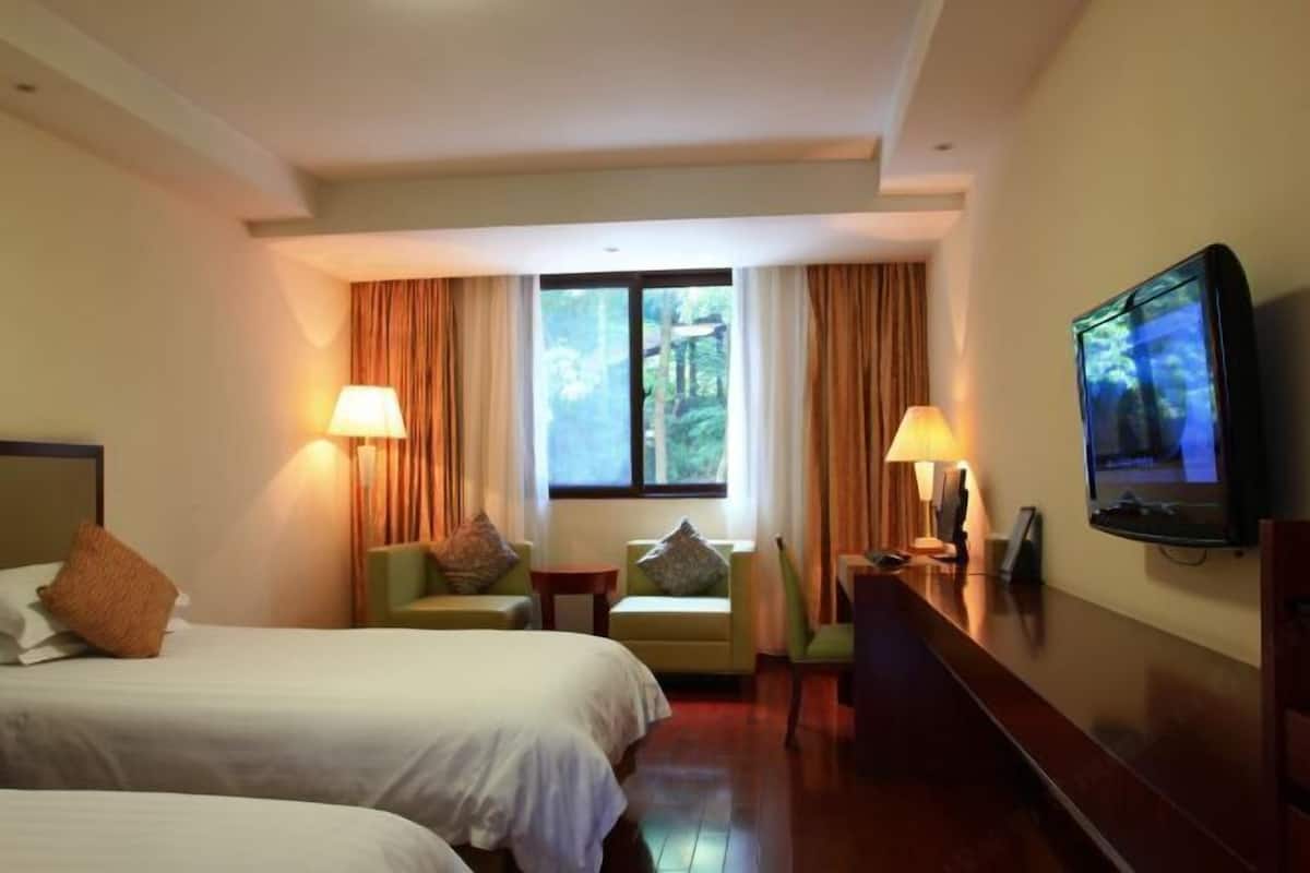 Habitación de hotel con dos camas, televisor, escritorio y ventana con cortinas.