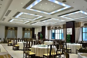 Un salón de banquetes con mesas redondas, sillas y un techo alto con iluminación empotrada.