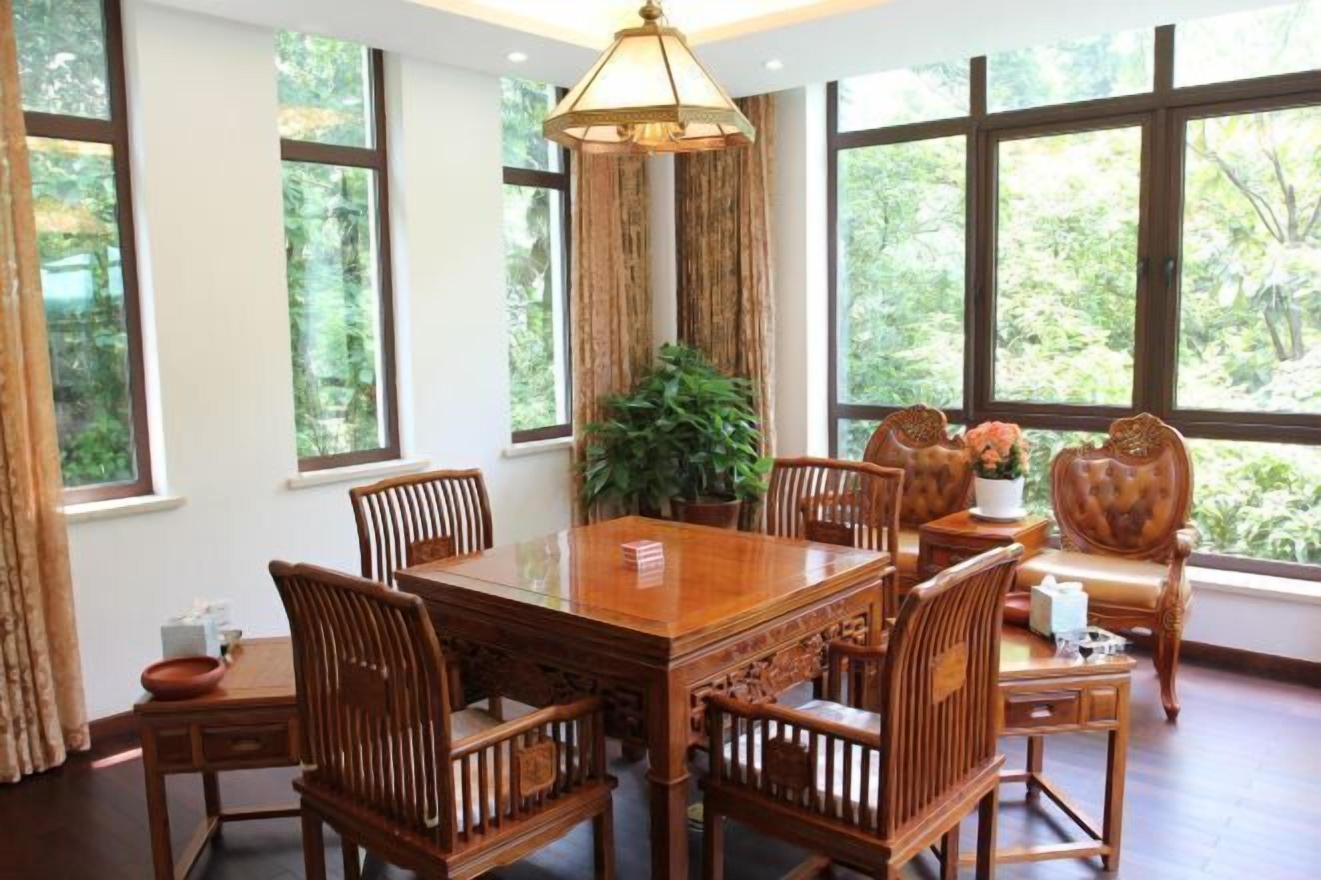 A dining area with a wooden table and chairs, large windows with a view of greenery, and a hanging light fixture.