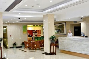 A hotel lobby with a reception desk, seating area, and a restaurant in the background. - Hupao Mountain Resort (Hangzhou)