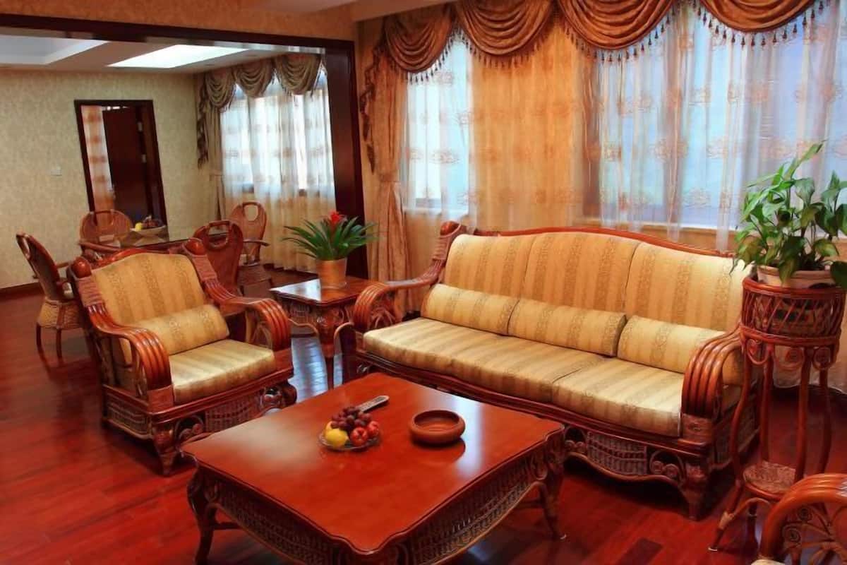 Un salón tradicional con sofá, sillones, una mesa de centro y cortinas.