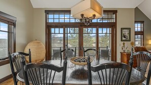 Un comedor con una mesa, sillas, una lámpara colgante y ventanas amplias con vistas.