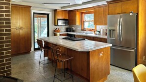 Eine moderne Küche mit Holzausstattung, einem Edelstahlkühlschrank, einer Mikrowelle und einer großen Kochinsel mit Barhocker.