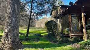 Eine Holzhütte mit Glastür, umgeben von bewaldeter Landschaft unter blauem Himmel.