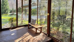 Eine Holzterrasse mit einer Bank und großen Fenstern, die einen Blick auf ein bewaldetes Gebiet bieten.