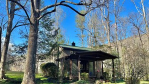 Eine rustikale Holzhütte mit Veranda, umgeben von Bäumen und einem gepflegten Rasen.