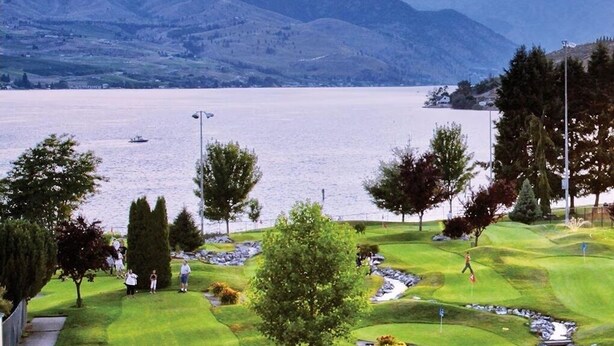 Een golfbaan met een meer en bergen op de achtergrond.