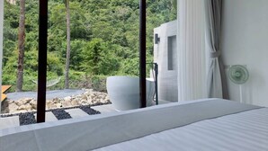 A bedroom with a large bed, a view of a lush forest, a white bathtub, and a green fan. - Red Cheek Mountain Villa (Ao Nang)
