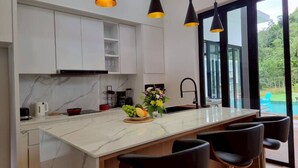 A modern kitchen with a marble island, black pendant lights, and a view of the outdoors. - Red Cheek Mountain Villa (Ao Nang)