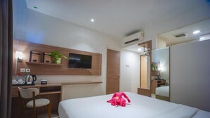 Una habitación de hotel con cama, escritorio, silla, televisión y espejo.