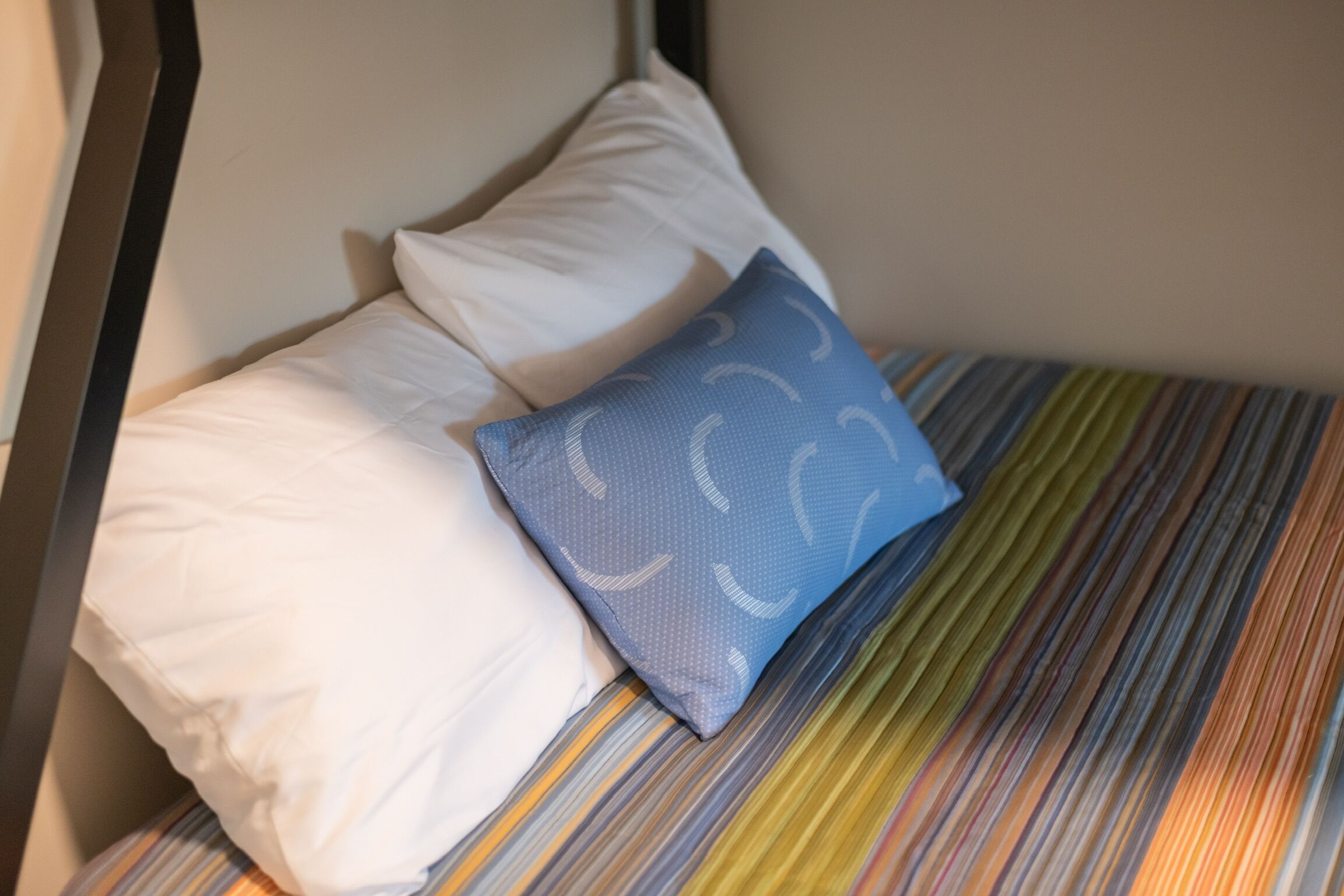 A bed with striped bedding, a white pillow, and a blue pillow with a pattern.
