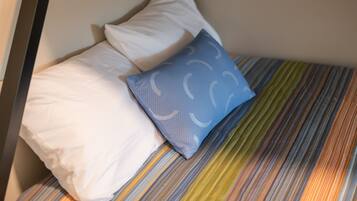A bed with striped bedding, a white pillow, and a blue pillow with a pattern.