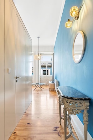 Ein Flur mit Holzboden, blauer Wand, rundem Spiegel und einem Tisch mit aufwendiger Tischbeinkonstruktion.