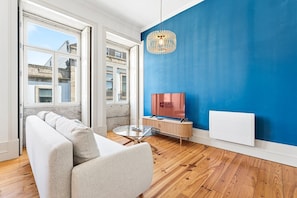 Ein modernes Wohnzimmer mit blauer Akzentwand, einem Sofa, einem Glastisch und einem Fernseher.