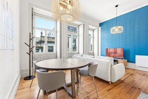 Ein modernes Wohnzimmer mit einem runden Tisch, grauen Sesseln, einem weißen Sofa und einem Fernseher, der 'GUEST READY' anzeigt.